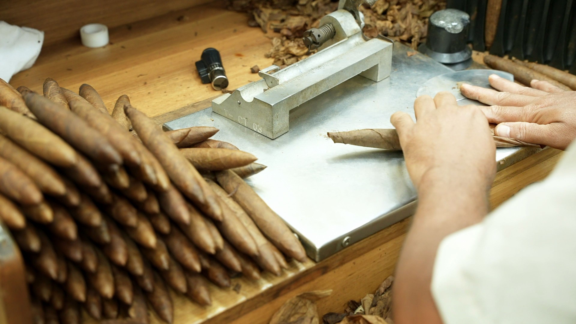 Close up of male hands making cigars from dry tobacco leaves on the rolling factory table. Cut, twist and gluing. The finished handmade product in stack
